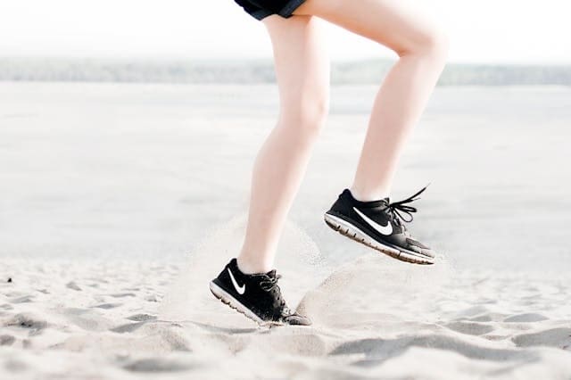 Aktive Joggerin auf Sand mit Nike Schuhen